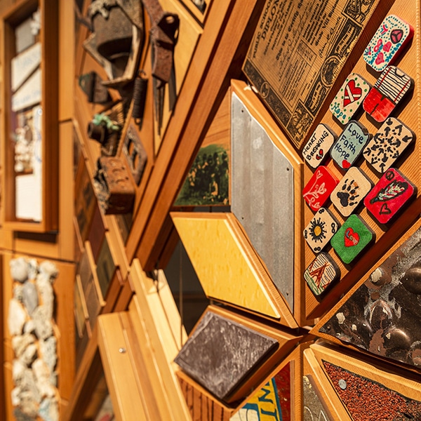 Éléments de bois peints, morceaux de quincailleries, cailloux et jouets rassemblés comme un témoignage sur un mur de bois.