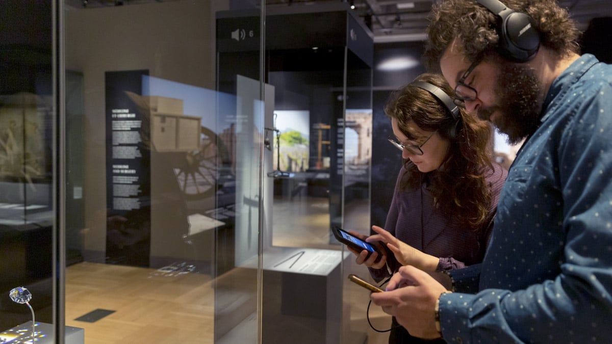 Visiteur et visiteuse utilisant l'application mobile comme audio-guide dans une exposition.