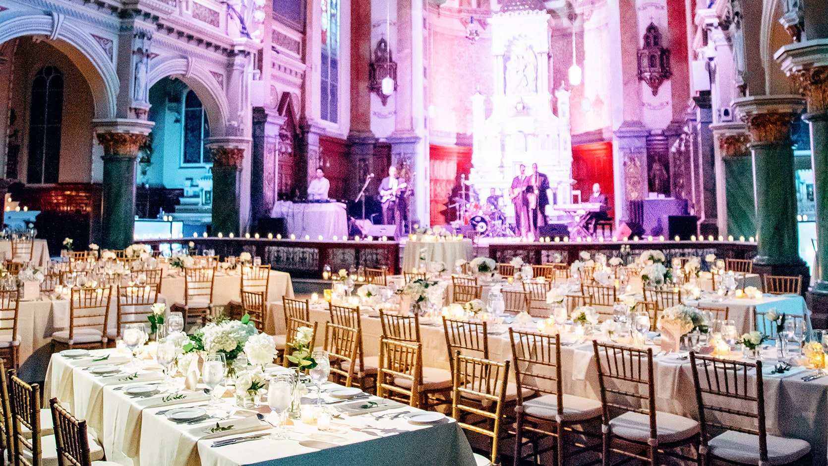 Chapelle du Séminaire de Québec en formule mariage avec des tables longues nappées en blanc, des chaises dorées et des arrangements floraux. Des musiciens répètent sur le coeur.