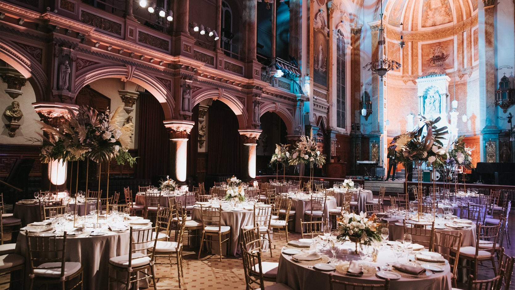 Chapelle du Séminaire de Québec en formule mariage avec des tables rondes nappées en doré, des chaises dorées et des arrangements floraux.