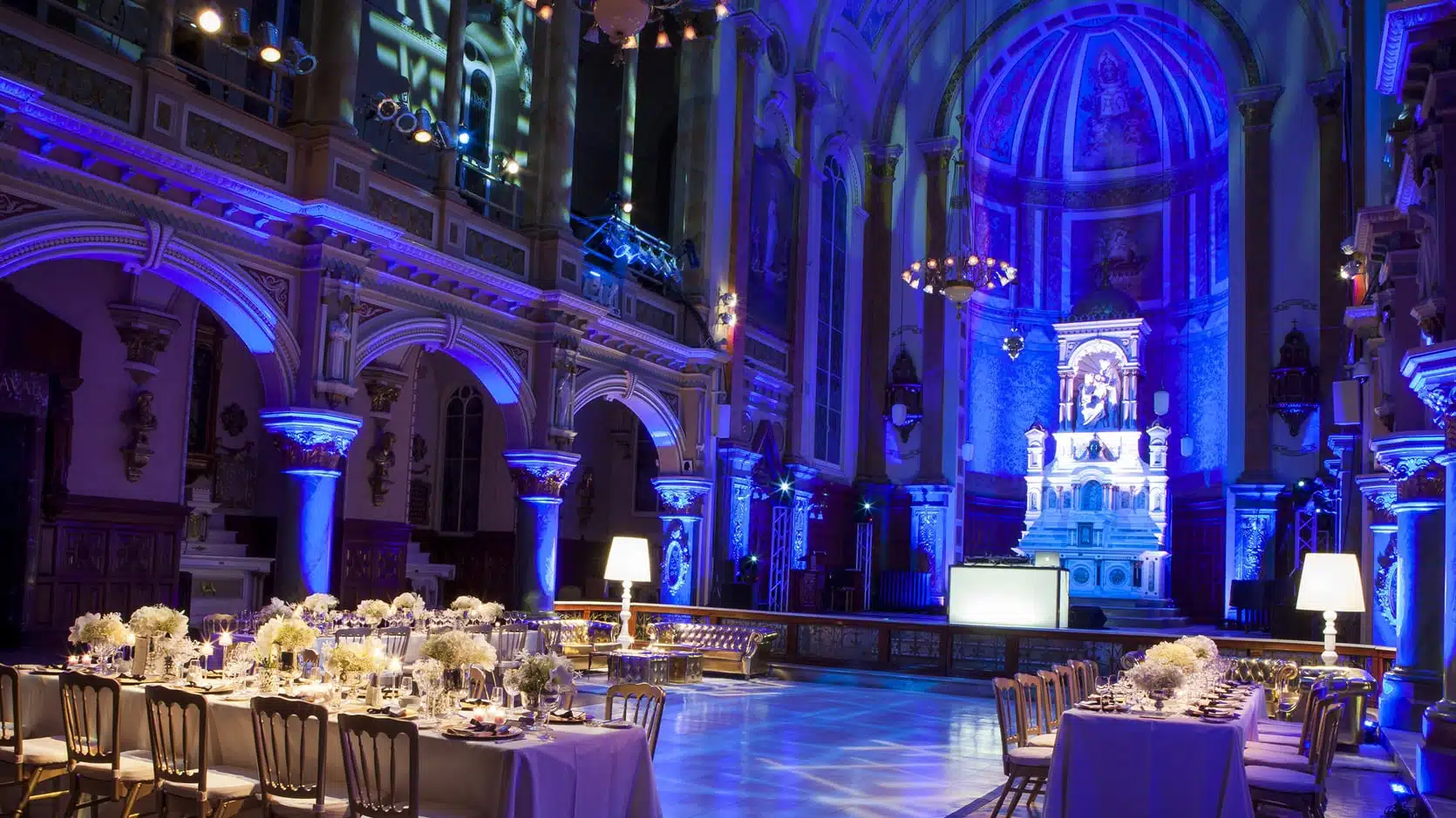 Chapelle du Séminaire de Québec en formule mariage avec des tables longue nappées en blanc, des chaises dorées et des arrangements floraux et une piste de dans au mileu.