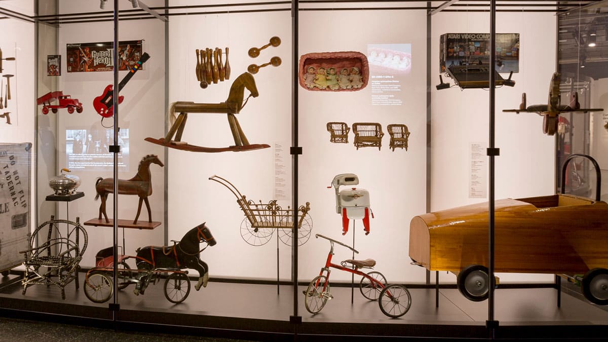 Vitrine regroupant plusieurs jouets de différentes époques : cheval à bascule, voiturette, tricycle, etc