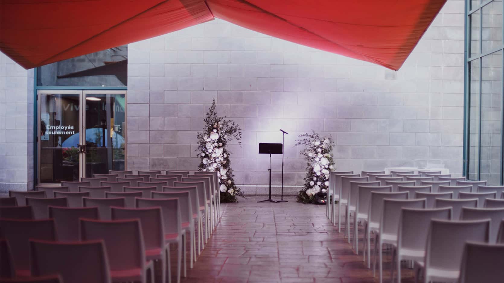 Dans la cour intérieur du Musée, des chaises sont placées le long d'une allée menant à deux arrangement floraux illuminés.