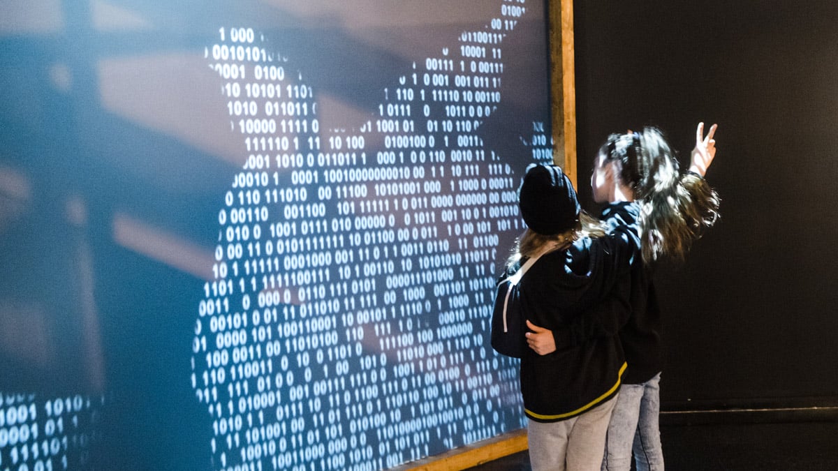 Deux jeunes abonnés du Musée s'amusent à faire réagir un mur de projection présentant du code binaire.