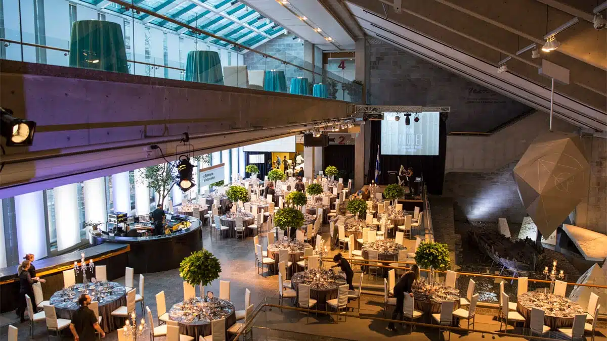 Le Hall du Musée en formule banquet, on y voit plusieurs tables rondes nappés en gris avec des chaises blanches et des arrangements floraux.
