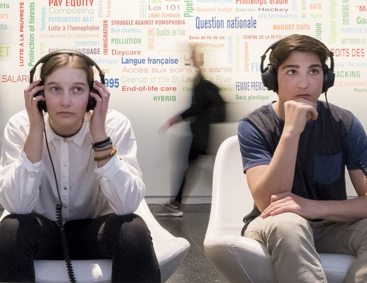 Deux jeunes adultes regardant une vidéo dans une exposition avec des écouteurs.