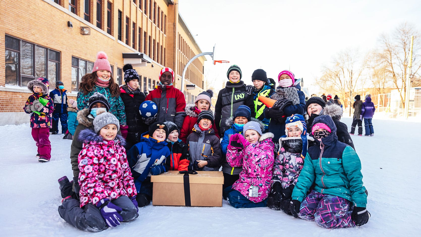 Enfants souriants dans leur cour d'école enneigée devant une boîtes surprise reçu dans le cadre d'une Journée Génération M