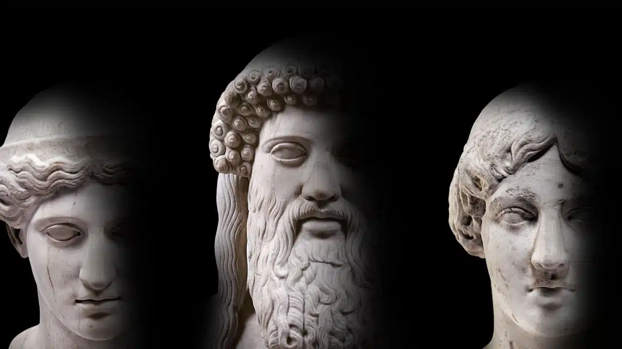 Trois visages de statues de marbre de dieux grecs dans la pénombre.