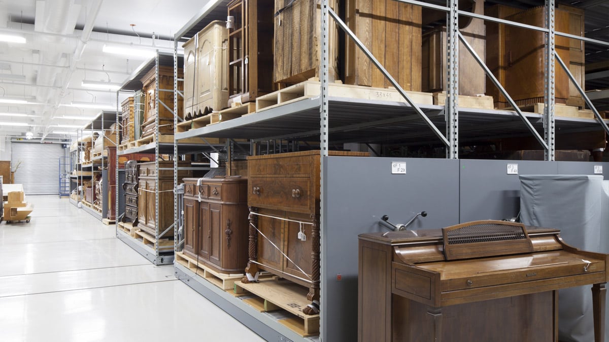 Vue d'ensemble de la réserve du mobilier en bois. Au premier plan un orgue et dans plusieurs tablettes des commodes, vaisseliers et autre bureaux en bois.