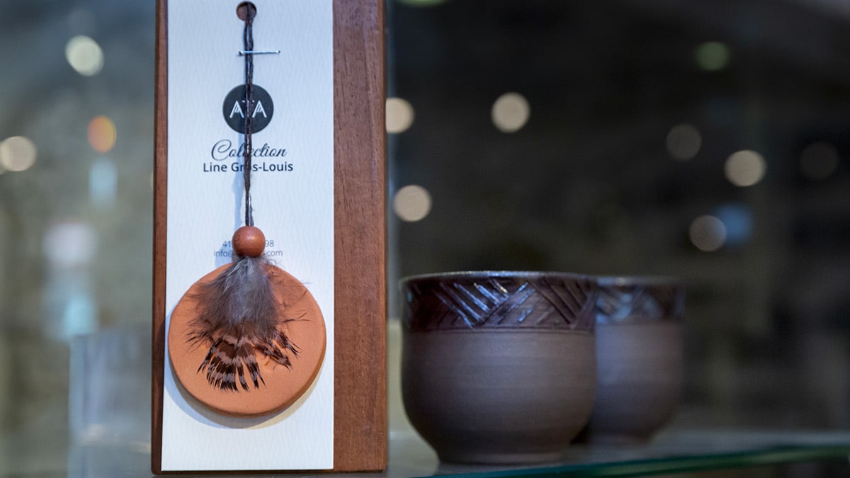 Artisanat autochtone en vente à la Boutique du Musée. Devant un pendentif en bois décoré une plume et derrière des verres à thé en argile.