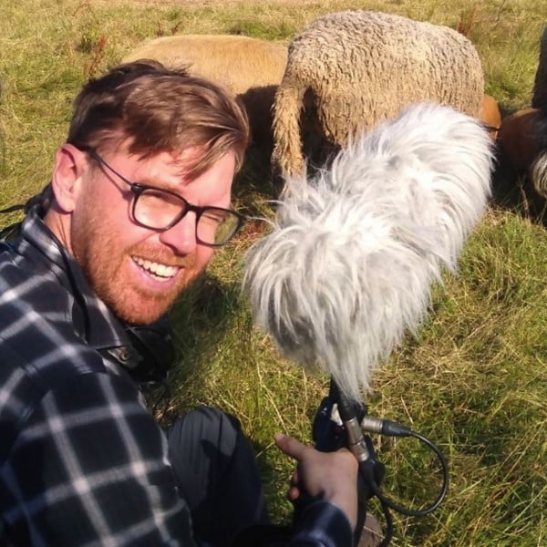Le réalisateur Oliver Dickinson en tournage, en compagnie de moutons dans un pré