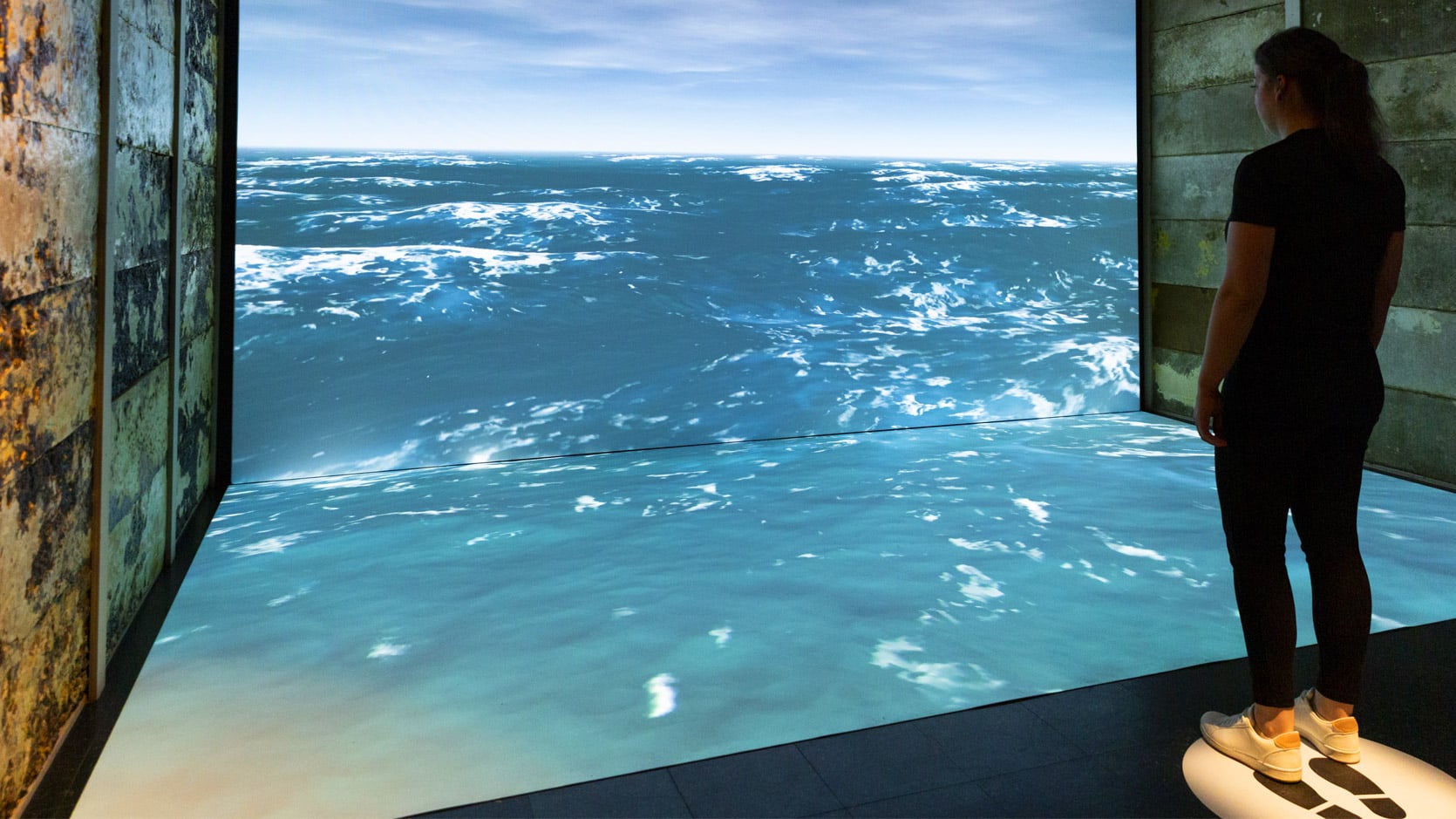 Une dame se tien devant une projection immersive d'un l'océan.