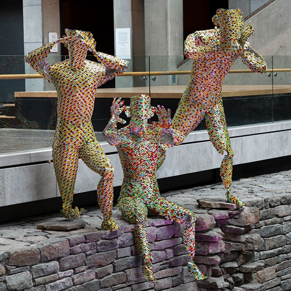 Trois personnages géants fabriqués avec des épinglettes multicolores sur le quai du Hall du Musée