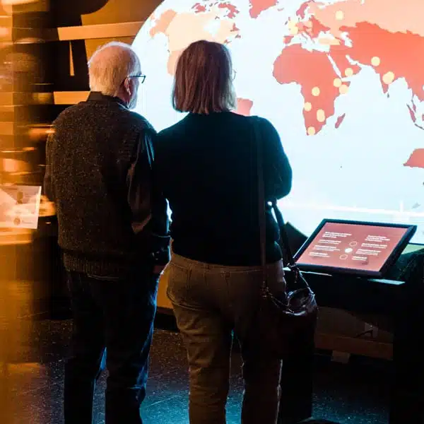 un homme et une femme vue de dos installés devant un écran et regardant une mappe monde électronique