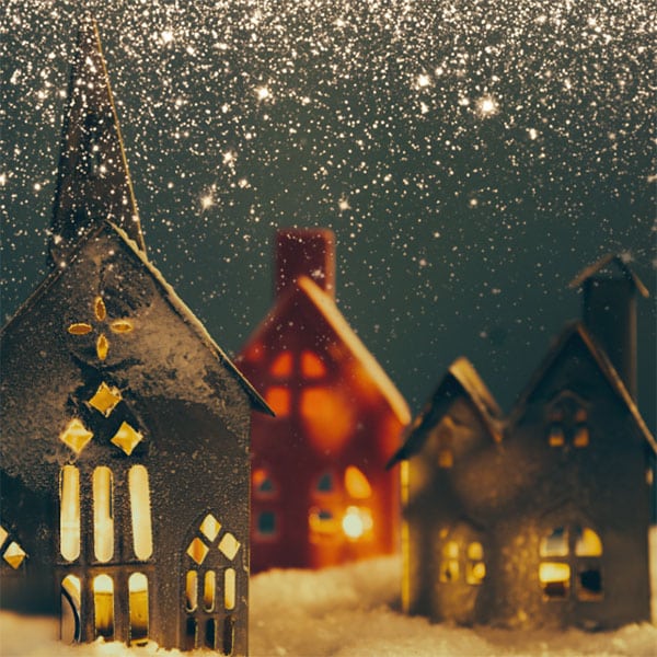 Deux maisons et une église en carton dans un paysage de Noël sous un ciel étoilé mêlé de neige