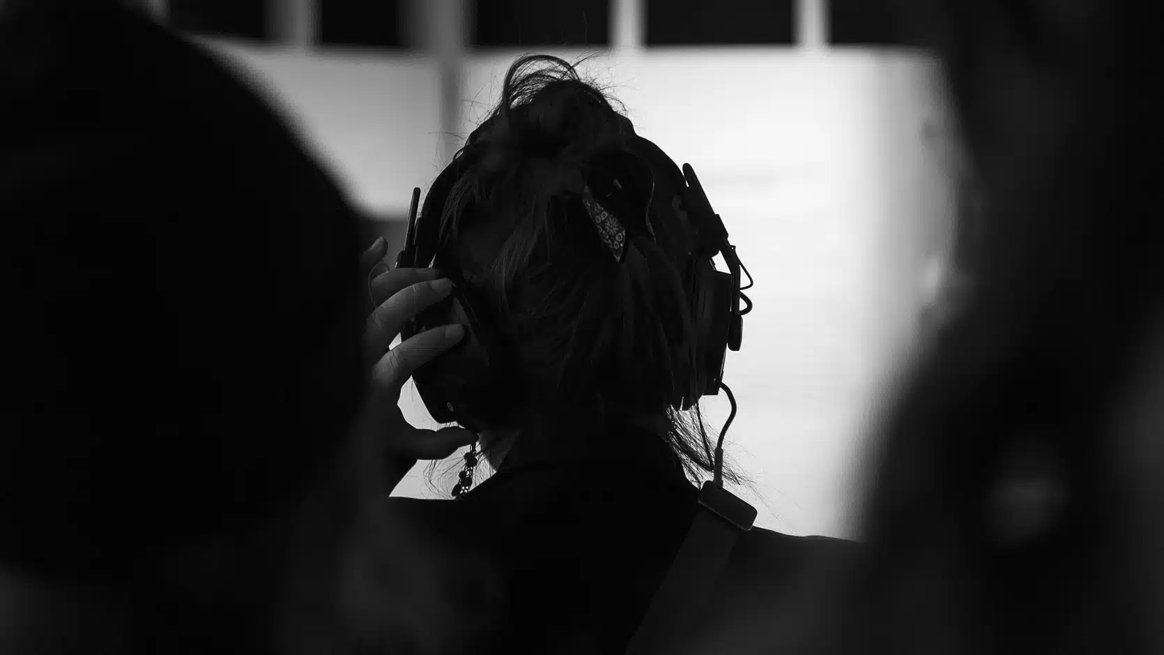 Photo en noir et blanc d'une personne de dos qui tient en place son casque d'écoute.