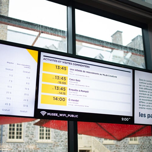 Photo des écran au dessus du comptoir d'information situé dans le Hall du Musée sur lesquels on voit l'horaire des activités du jour