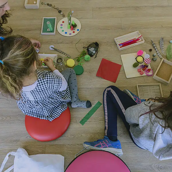 deux fillettes assises au sol qui font du bricolage photographiées de dos. vue en plongée