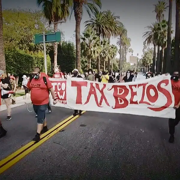 photo d'une manifestation dans une rue de Californie où les manifestants tiennent une banderole rouge et blanche contre la taxe Bezos, fondateur d'Amazon