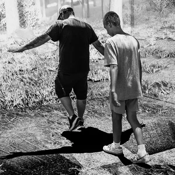 photo noir et blanc de deux hommes en short longue et t-shirt marchant sur du gazon prise de dos