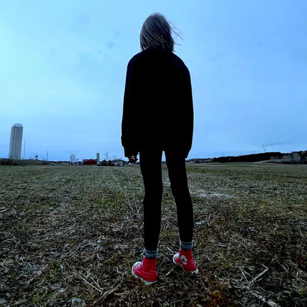 photo d'une femme habillée en noir avec des baskets rouge Converse prise de dos dans un champ agricole