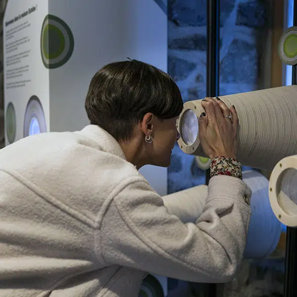 une femme aux cheveux foncés et courts regarde à travers un genre de téléscope en carton