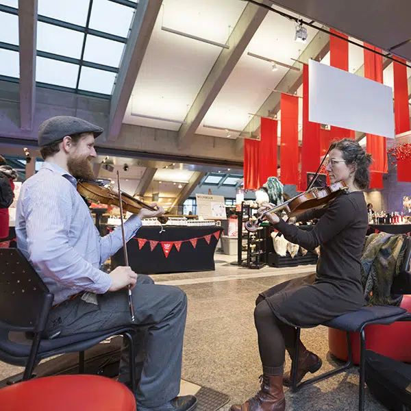 un homme et une femme jouant du violon sont assis face à face dans le hall du Musée de la civilisation à Québec