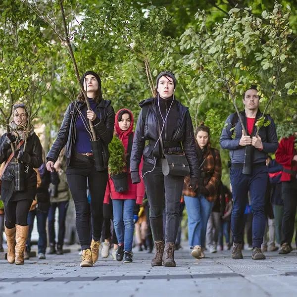 photographie couleur tirée du film Je me soulève où l'on voit un groupe d'hommes et de femmes marcher sur un trottoir dont plusieurs tiennent des brances d'arbres à la main