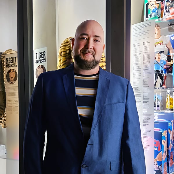 Jean-François Leduc en veston bleu devant deux des vitrines présentant ses objets de collection de lutte