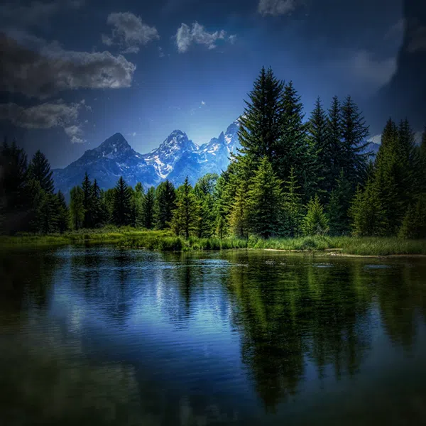 image d'un paysage d'un lac avec en arrière-plan une forêt et une chaîne de montages sous un ciel bleu avec des nuages