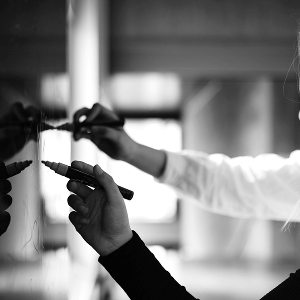Photo noire et blanc de deux mains qui écrivent sur un tableau noir