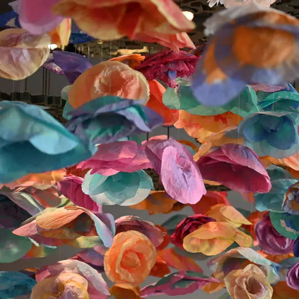 Photographie qui montre un amas de fleurs en papier multicolores suspendues