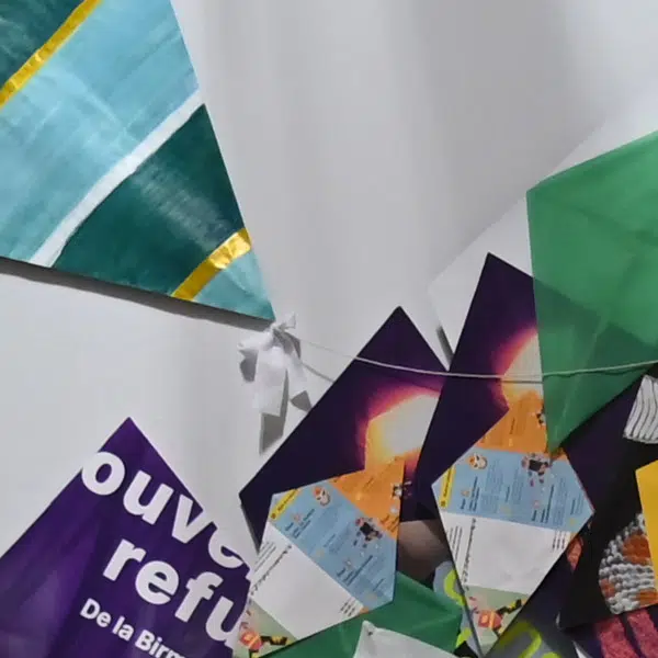 photographie couleurs d'un montage de cerfs-volants faits avec différents types de papier aux imprimés variés avec notamment l'affiche de l'exposition Trouver refuge