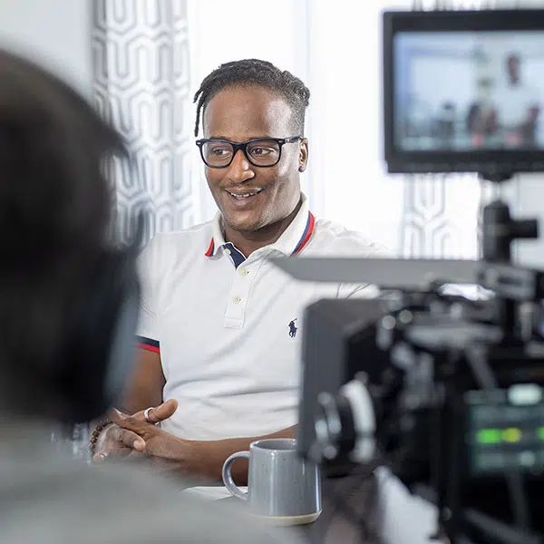 Photo couleurs de Jérémy Jean-Baptiste, chef cuisinier et animateur, captée lors du tournage du documentaire Des immigrants et des papillons, assis à une table avec devant la caméra