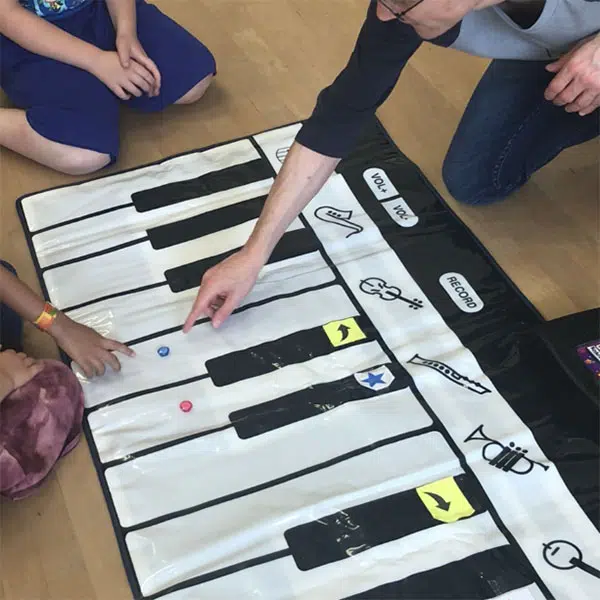 deux enfants et un adulte accroupis autour d'un clavier de piano format géant bricolé avec du papier glacé