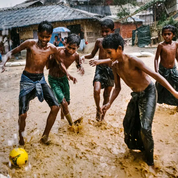 image issue du film Errance sans retour. Elle montre 5 garçons torse nu en train de jouer au soccer sous la pluie dans un camp de réfugiés.