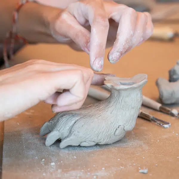 Photographie qui montre une patte d'ours en argile en train d'être sculptée par des mains