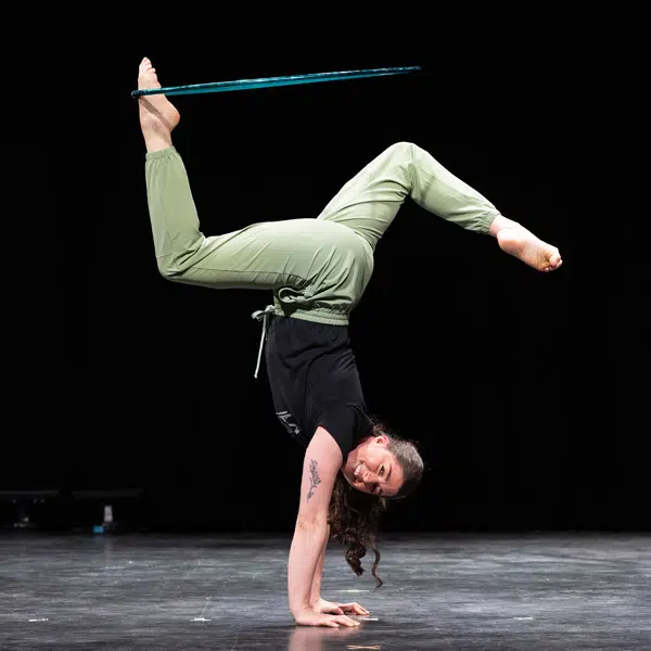 Photographie qui représente une fille sur les mains en train de jouer avec un cerceau avec son pied.