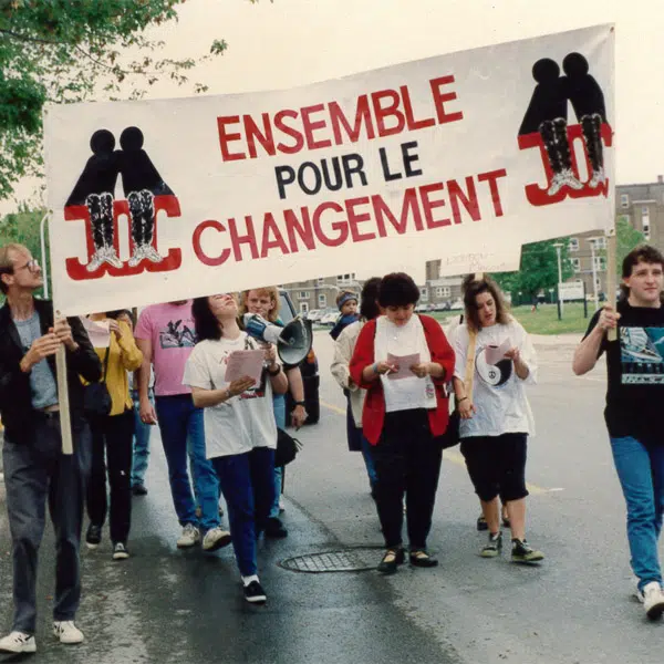 Photographie qui représente un groupe de jeunes personnes en train de manifester dans la rue avec une affiche où il est inscrit : "JOC - Ensemble pour le changement"