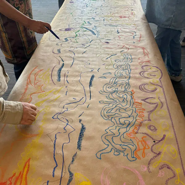 photo d'une longue feuille de papier en train d'être dessinée par plusieurs mains pour réaliser un œuvre collective