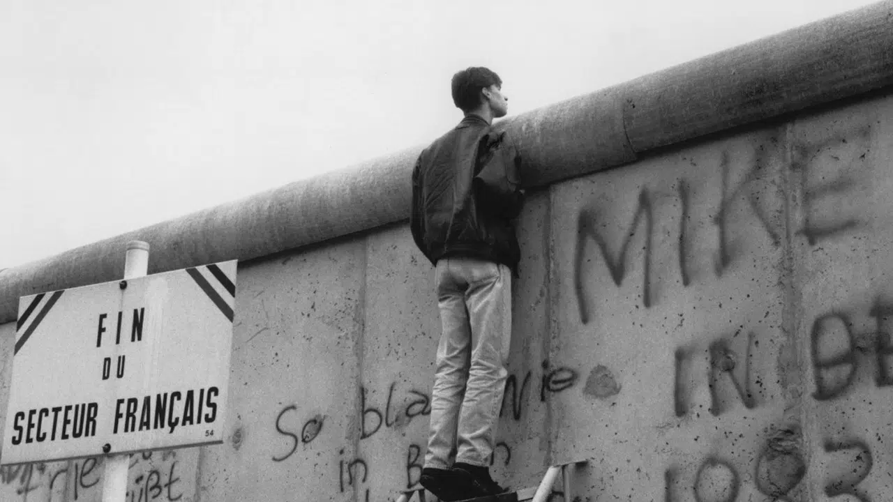 Photo en noir et blanc d'une personne qui regarde par-dessus le mur de Berlin